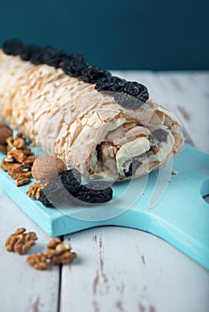 Prune-nut meringue roll on a blue cutting board on a white vintage wooden kitchen table