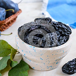 Prunes in a clay bowl and fresh plums, leaves on a table.