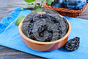 Prunes in a clay bowl and fresh plums, leaves on a wooden table