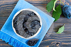 Prunes in a clay bowl and fresh plums, leaves on a wooden table.