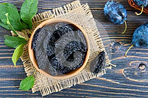 Prunes in a clay bowl and fresh plums, leaves on a wooden table