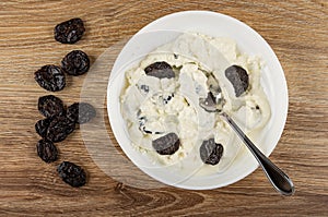 Prunes, plate with mix of cottage cheese, sour cream, dried plum, spoon on table. Top view
