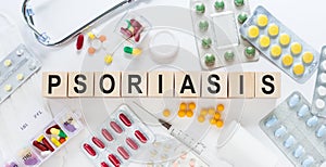 PSORIASIS word on wooden blocks on a desk. Medical concept with pills, vitamins, stethoscope and syringe on the background
