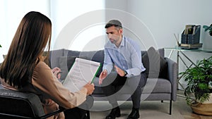 Psychologist listens client taking notes on clipboard at psychotherapy session