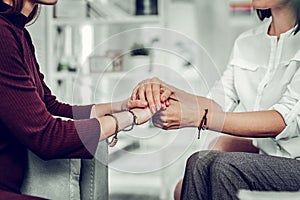 Psychologist wearing white shirt and bracelets holding hands of client photo