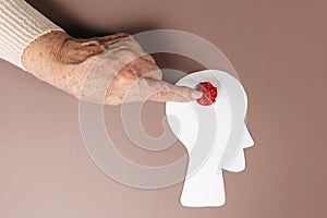 Psychology and mental heaslth. The hand of an elderly woman points to a braided red ball in the silhouette of the head