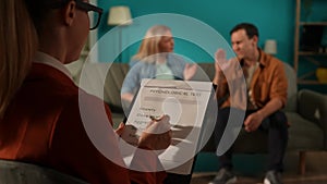 A psychotherapist administers a psychological test to the couple, taking notes. A clipboard with a psychological test in