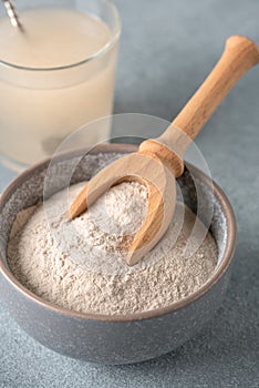 Psyllium husk powder in bowl close-up and glass with of water soluble fiber for intestinal, gray background. Gluten free diet