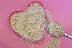 Psyllium in the shape of a heart on a pink background, top view. Super food psyllium seeds, keto diet ingredient