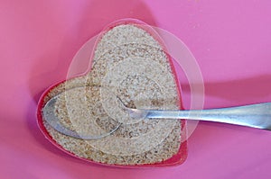 Psyllium in the shape of a heart on a pink background, top view. Super food psyllium seeds, keto diet ingredient