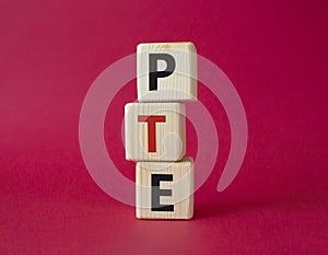 PTE - Pearson Tests of English symbol. Wooden cubes with word PTE. Beautiful red background. Business and PTE concept. Copy space