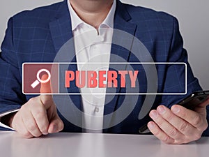 PUBERTY text in search line. Modern Banker looking for something at smartphone. PUBERTY concept