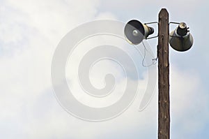 Public address horn loud speakers on wooden pole over blue sky