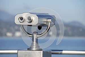 Public binocular on sea shore, close up. Coin operated binocular viewer on blurred background of sunset and sea