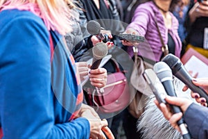 Public figure talking to the media, journalists holding microphones at press conference