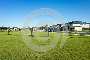 A public park with green lawn/grass and young trees surrounded by new residential houses/Australian homes in a Melbourne`s suburb