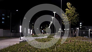 Public park infrastructure and night lighting. Stock footage. Man walking through green alley in the city park near