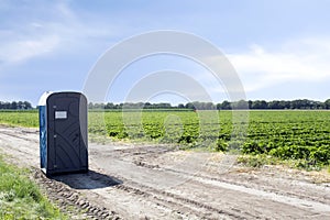 Public plastic portable toilet on agriculture field of farmer landscape with blue sky, outdoors