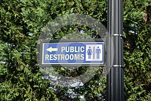 Public Restrooms Sign on a black pole with evergreen tree in background