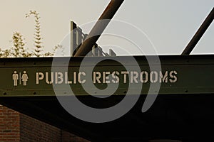 Public restrooms sign on a green metal structure in a clear sunset.