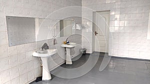 Public toilet with a mirror, two washbasins and white tiles