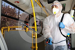 Public transport sanitation. Worker in suit disinfecting bus salon, focus on spray machine nozzle