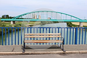 Public wooden bench with wrought iron legs and old metal arched railway bridge in background