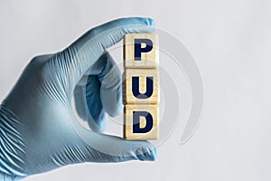 PUD is an acronym on cubes held by a hand in a blue glove