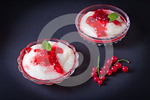 Pudding from semolina in a glass bowl with red currant syrup and berries. On a dark background