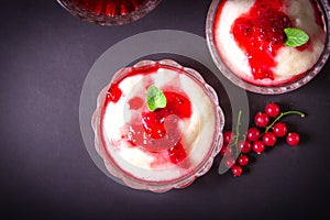 Pudding from semolina in a glass bowl with red currant syrup and berries. On a dark background