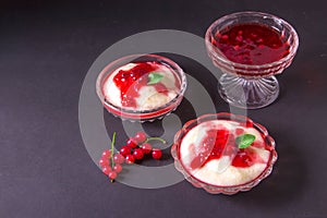 Pudding from semolina in a glass bowl with red currant syrup and berries. On a dark background