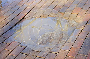 Puddle with dirty snow in a dent in clinker pavement photo