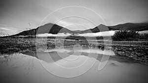 Puddle of rain with reflection in the front. Mountain with fog i