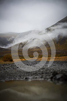 Puddle of rain with reflection in the front. Mountain with fog i