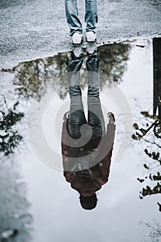 Puddle with reflection of girl walking with backpack