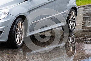 Puddle on the sidewalk with a reflection of a parked car, closeup, road after rain