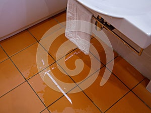 A puddle of water on orange tiled floor in room. Flooded production. Water leak in toilet or bathroom.