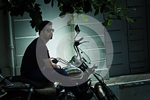 Puducherry, South India: An adult Indian male bike rider with beard in sunglasses on a motor bike / cruiser bike parked by the