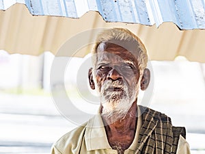 An unidentifed old senior indian poor man portrait with a dark brown wrinkled face and white hair and a white beard, looks serious