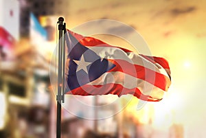Puerto Rico Flag Against City Blurred Background At Sunrise Back