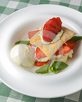 Puff pastries with strawberries and berry sauce on a white plate. Over green plaid background.