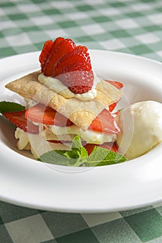 Puff pastries with strawberries and berry sauce on a white plate. Over green plaid background.