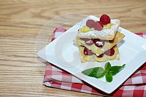 Puff pastry cake with mint leaves and raspberries in a white plate, background with copy space