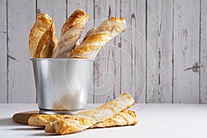 Puff pastry cheese sticks in a metal bucket on a light background