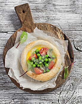 Puff pastry egg tartlet with fresh green peas and cherry tomatoes on wooden rustic board.