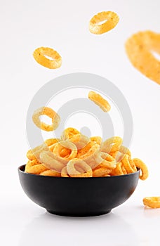 Puffed corn rings chips in black bowl on white background