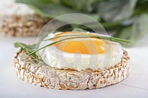 Puffed exploded wheat grains with fried egg and spinach leaves on a light wooden background.