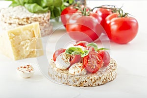 Puffed exploded wheat grains with slices of mozzarella and chili tomato sprinkled with pepper on a light wooden table