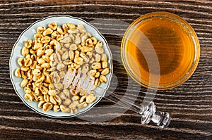 Puffed wheat in saucer, honey dipper, bowl with honey on table. Top view