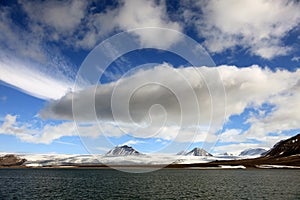 Puffy white clouds, blue sky, mountain peaks and glaciers in the arctic Svalbard